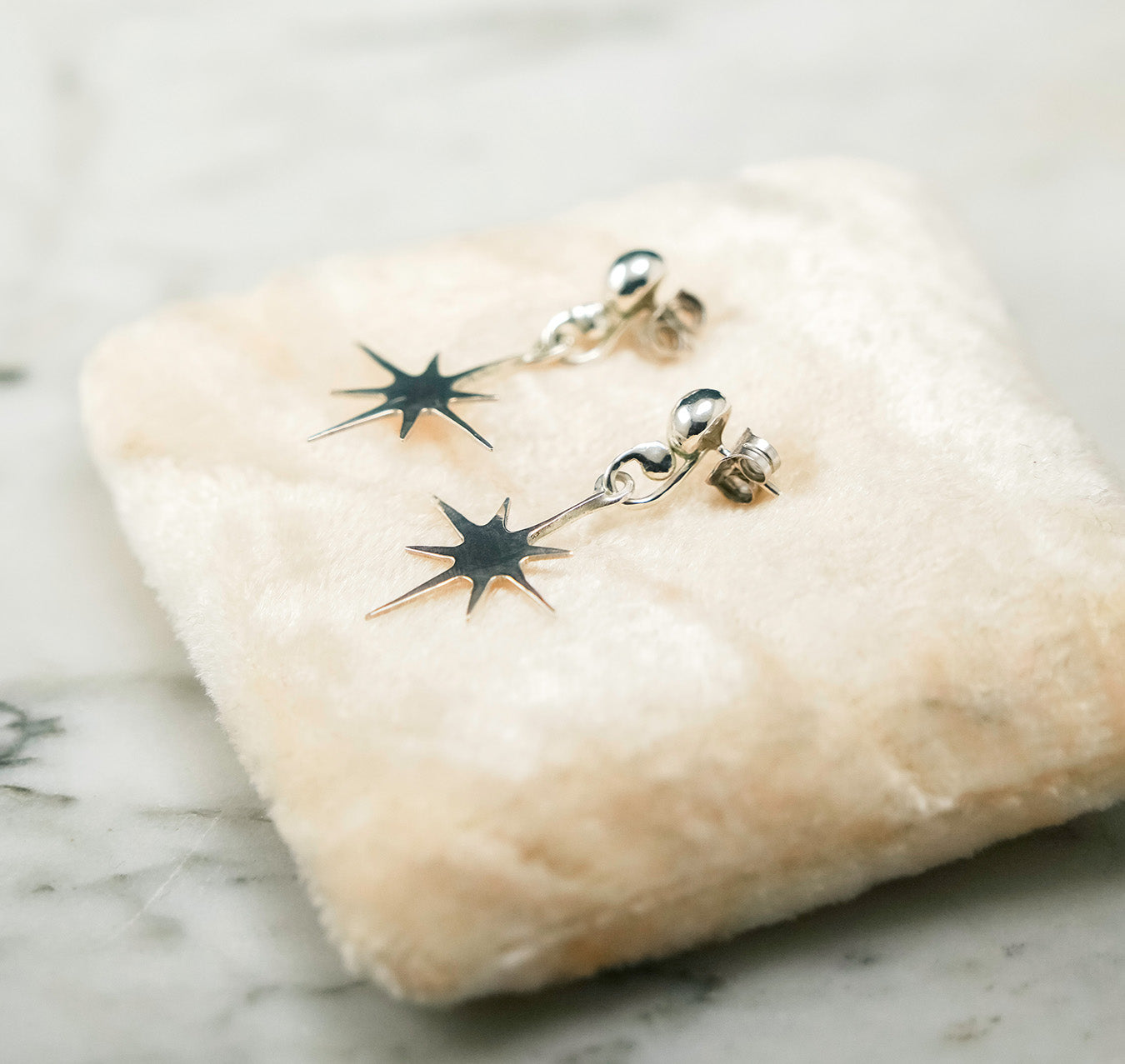 
                  
                    Star-shaped earrings on a textured stone surface
                  
                